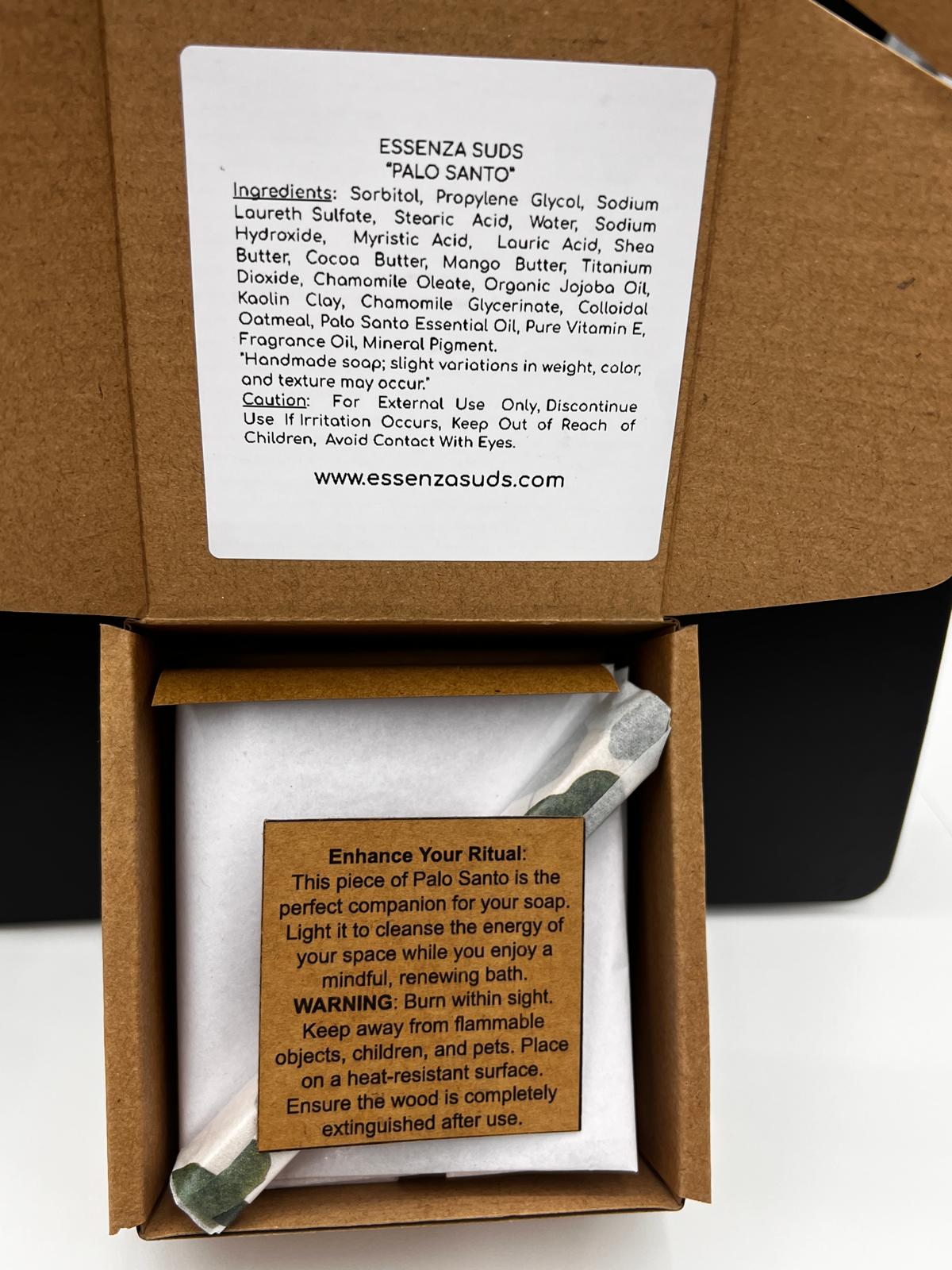 This image shows the thoughtful, cardboard packaging for our Palo Santo handmade soap by Essenza Suds., you'll see your soap snugly wrapped in protective white tissue paper. Also included and wrapped is a genuine Palo Santo smudging stick, accompanied by an informative card labeled "Enhance Your Ritual." This card explains how to burn the wood to cleanse your space's energy, transforming your bath time into a mindful, renewing experience.